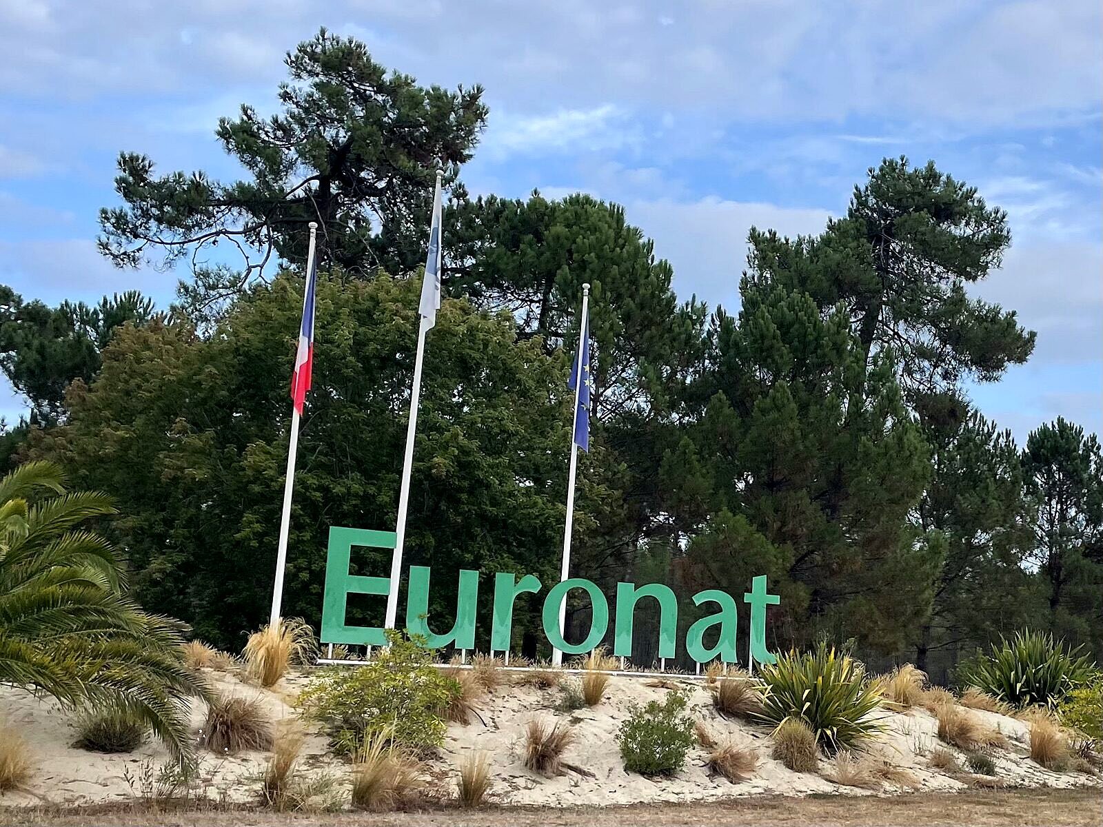 Euronat-Eingangsschild mit Pinienwald und drei Fahnen am Camp-Eingang
