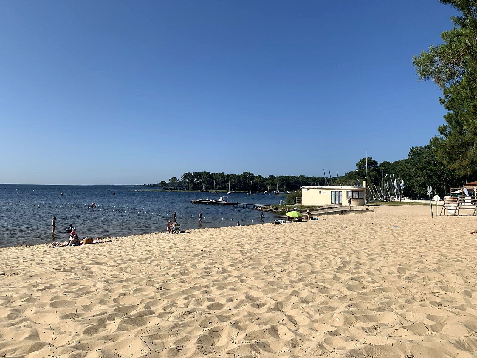 Plage de Piqueyrot am Lac d'Hourtin: flacher Sandstrand, Segelboote am Steg, im Hintergrund Pinienwald
